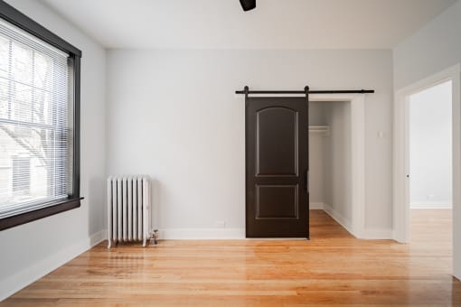 a room with a wood floor and a black door and a radiator and a window