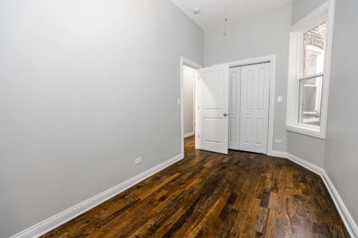 a bedroom with white walls and wood flooring and a door to a closet
