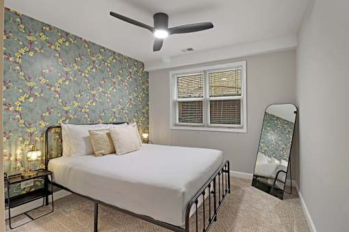 A bedroom with a bed, a fan, and a floral wallpaper.