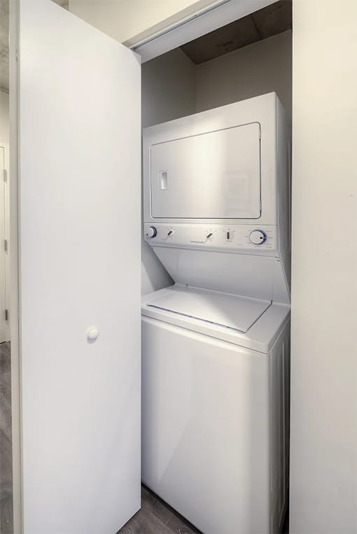 A white dryer is in a small space next to a white door.