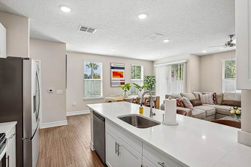A kitchen with a refrigerator, sink, and a couch in the background.
