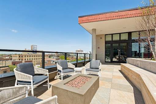 A patio with chairs and a fire pit on a rooftop.