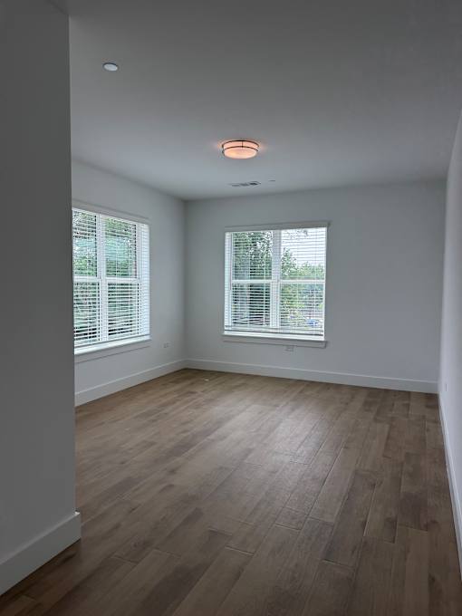 A room with wooden flooring and two windows with blinds.