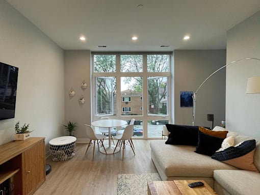 A modern living room with a white sofa, a wooden coffee table, and a large window with a view of a building outside.
