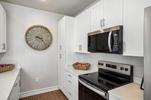 A kitchen with a stove, microwave, and clock on the wall.