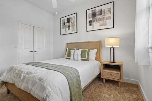 A bedroom with a bed, nightstand, and two framed pictures on the wall.