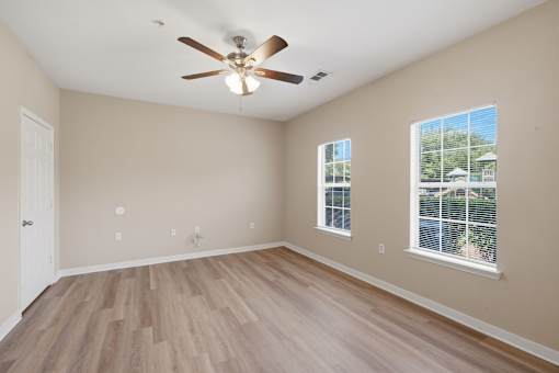 A room with a ceiling fan and two windows.