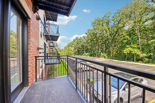 A balcony with a black railing and a view of a parking lot and trees.