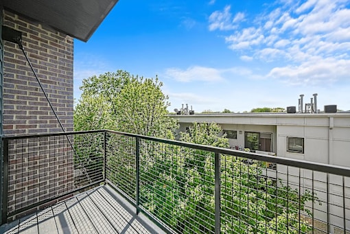A balcony with a black railing overlooks a green yard and a building.