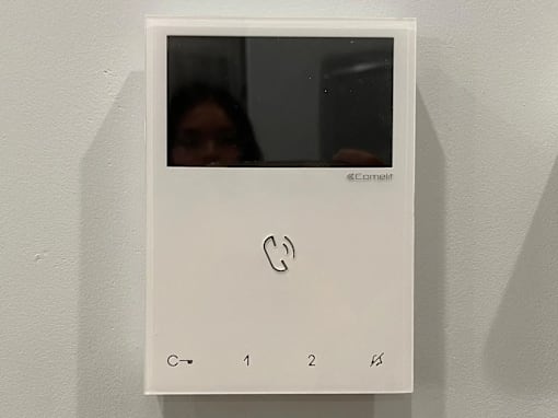 A white phone mounted on a wall with a woman in the background.