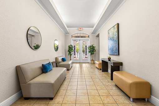 A hallway with beige couches and a round mirror on the wall.