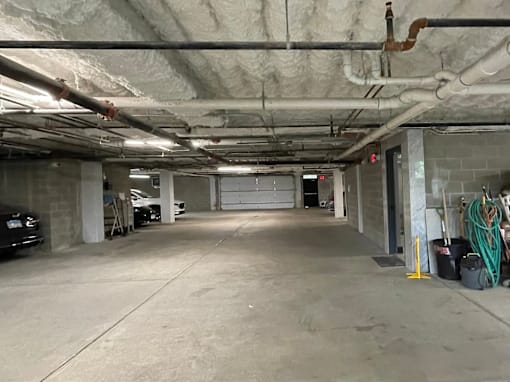 A large, empty garage with a concrete floor and walls, and a car parked on the left side.