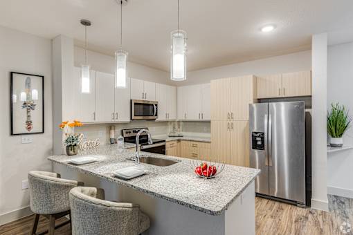 A modern kitchen with a central island, chairs, and a refrigerator.