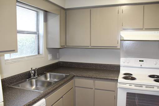 A kitchen with a stove, sink, and cabinets.