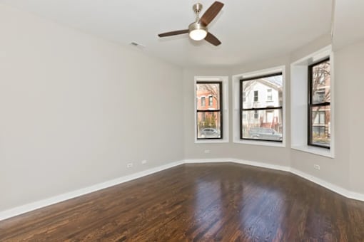 A room with a ceiling fan and three windows.