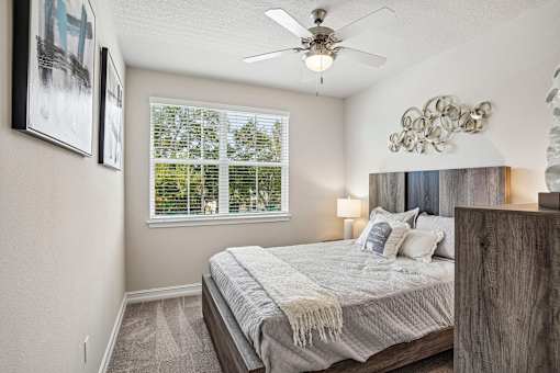 A bedroom with a bed, a ceiling fan, and a window with blinds.