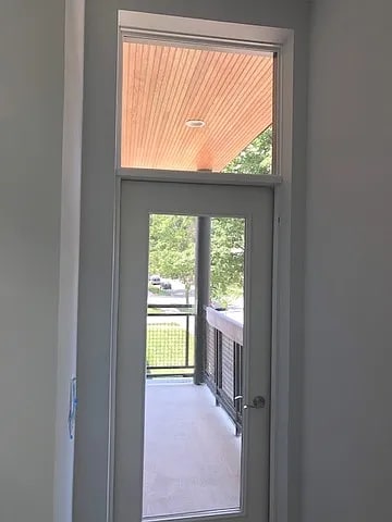 A doorway leading to a balcony with a view of a parking lot.