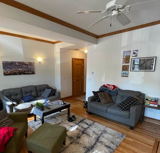 A living room with a grey couch, a green ottoman, a coffee table, and a ceiling fan.