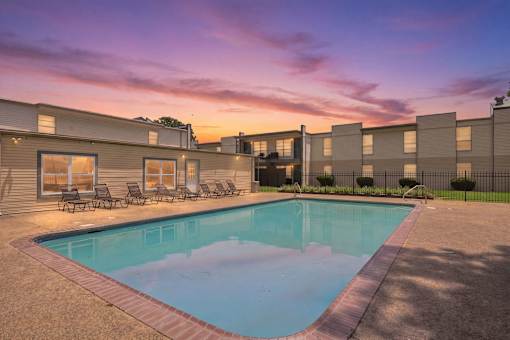 A swimming pool surrounded by a concrete patio and lounge chairs.