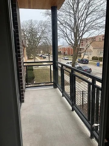 A balcony with a black railing and a view of a street with cars and houses.