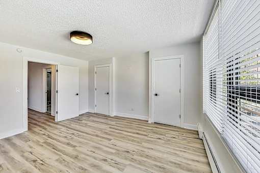 A room with white walls and wooden flooring with a window on the right side.