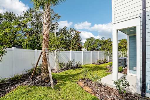 A white fence surrounds a tree and shrubs in a yard.