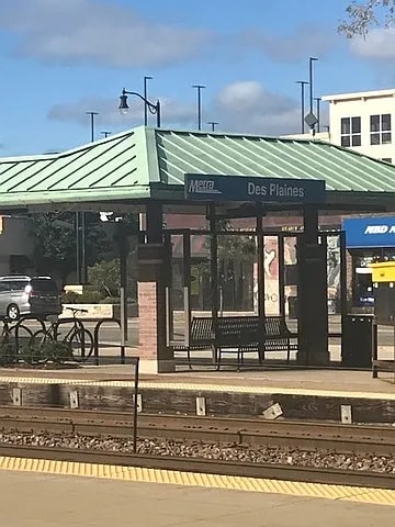 A train station with a green roof and a sign that says Des Plaines.