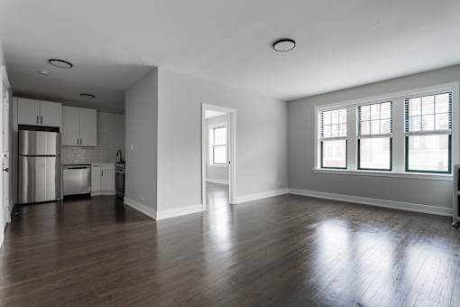 A large empty room with wooden floors and a window with white blinds.