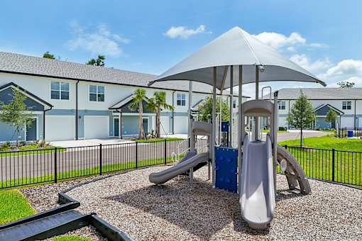 A playground with a slide and a canopy is in front of a building.
