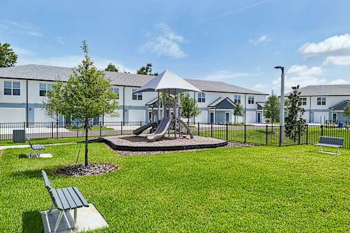 A playground area with a slide and a tree in front of apartment buildings.