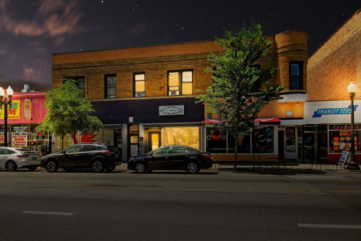 a city street at night with cars parked in front of a building