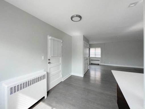 an empty living room with a white door and a kitchen