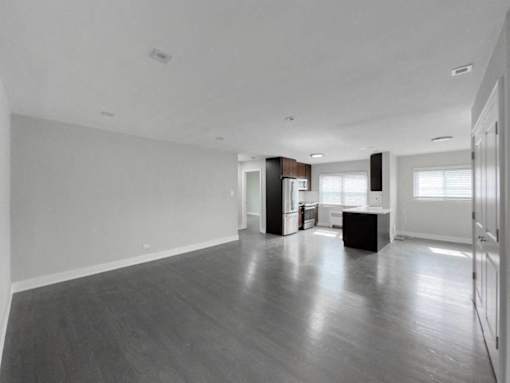 an empty living room with a kitchen and a refrigerator