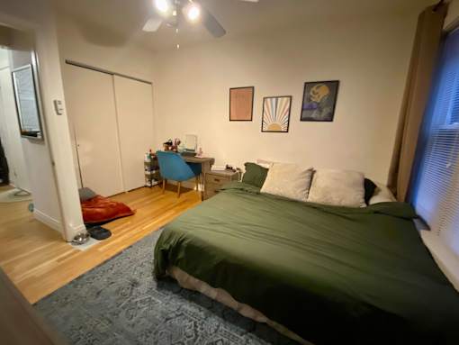 A bedroom with a bed, desk, chair, and a ceiling fan.