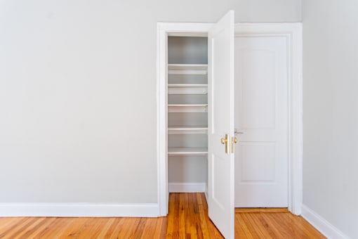 A white door with a gold handle is open to a white wall and a white shelving unit.