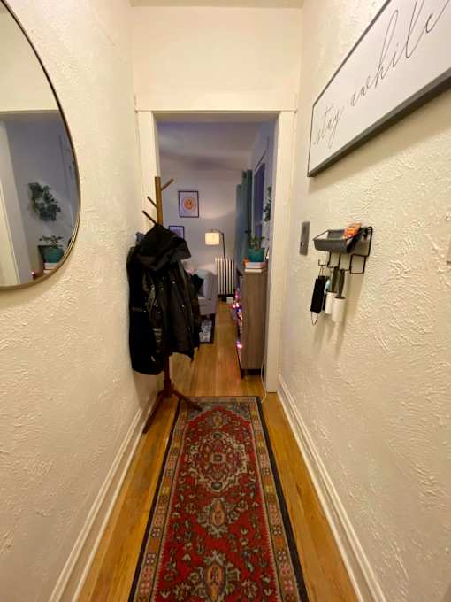 A hallway with a rug on the floor and a coat hanging on the wall.