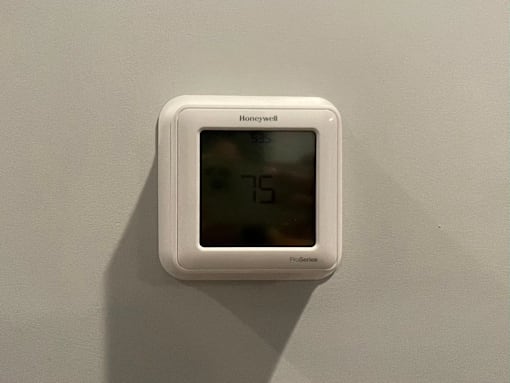A white Honeywell thermostat is mounted on a white wall.