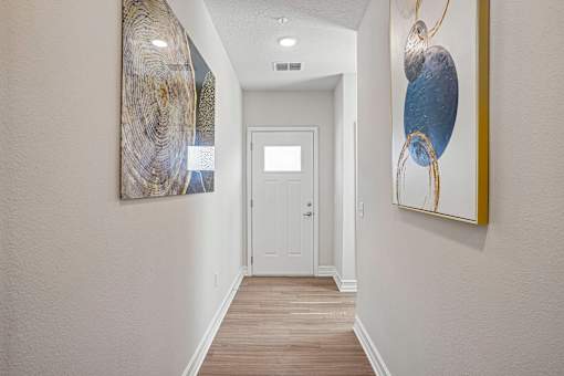 A hallway with a white door and two paintings on the wall.
