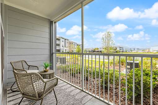 A balcony with a chair and table overlooking a green area.