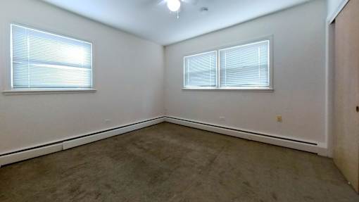 A room with a carpeted floor and two windows.
