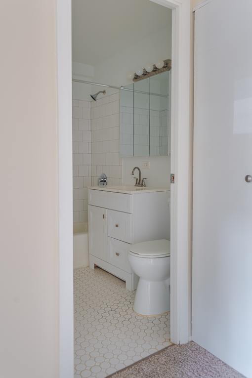 A white toilet sits in a bathroom with a white sink and a white cabinet.