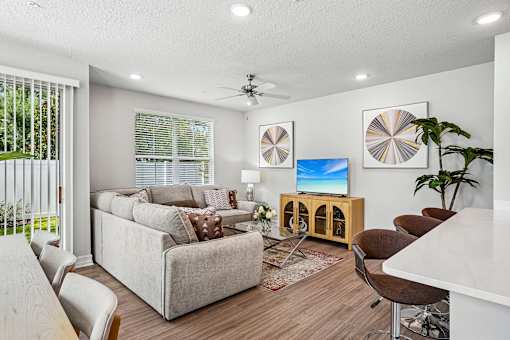 A living room with a grey couch, a television, and a ceiling fan.