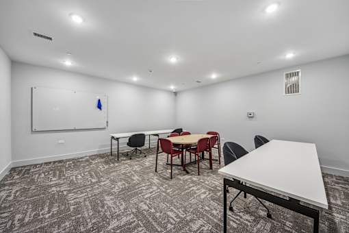 A room with a white table and chairs, a whiteboard, and a blue object on the whiteboard.