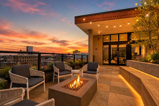 A patio with a fire pit and chairs is set against a sunset sky.