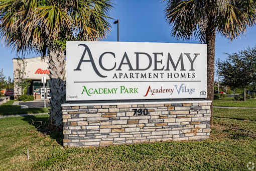 A stone sign for Academy Park Apartment Homes stands in front of a palm tree.
