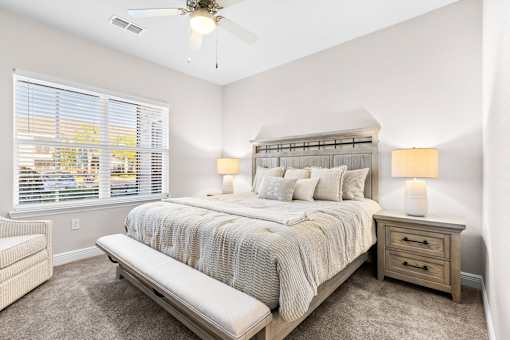 A bedroom with a large bed, a bench, and a ceiling fan.