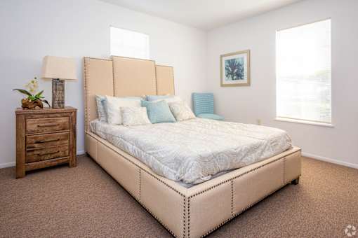 A bedroom with a large bed, a wooden nightstand, and a window.