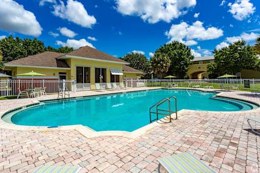 A swimming pool surrounded by a brick patio and a yellow building in the background.