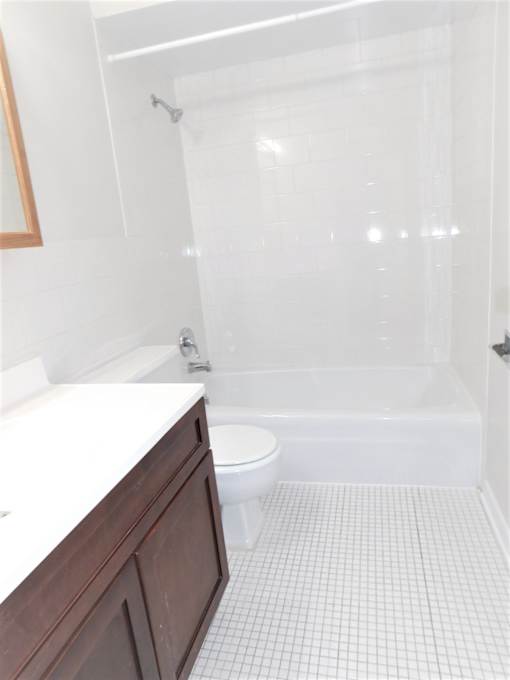 A white tiled bathroom with a toilet, sink, and shower.