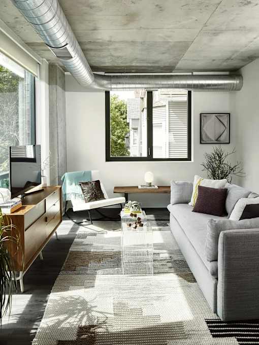 A modern living room with a grey couch, a wooden cabinet, and a large window.